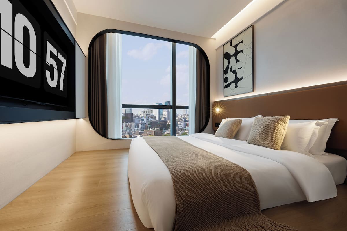 Une chambre d’hôtel moderne dotée d’un grand lit, offrant une vue sur la ville et présentant un décor mural original.