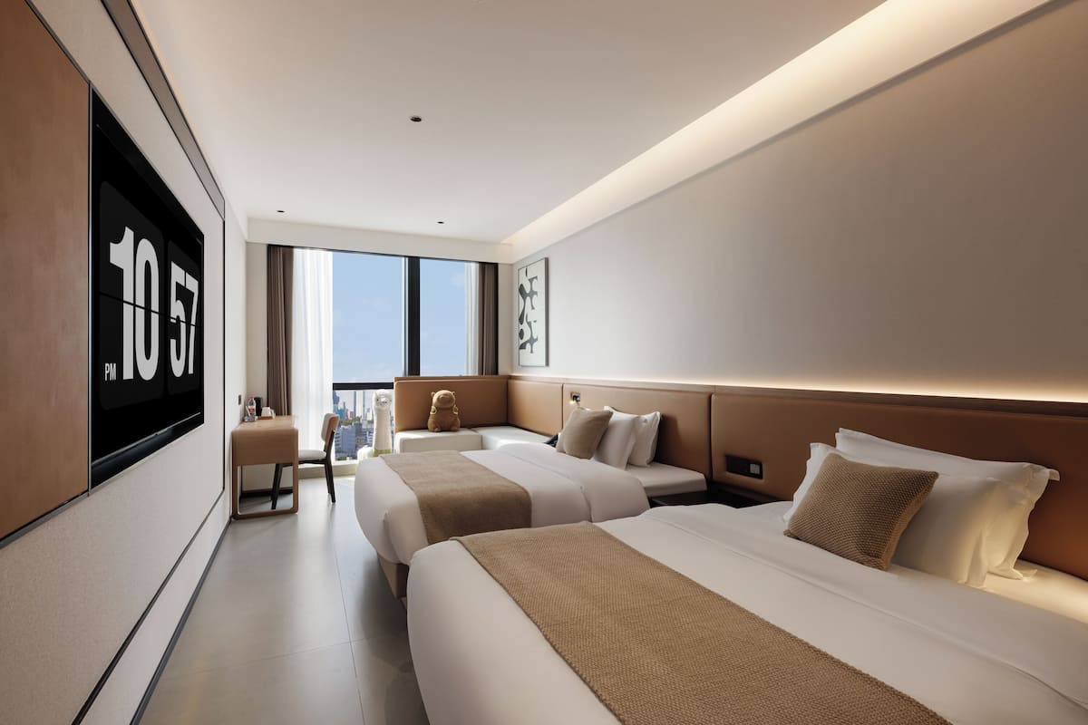 Une chambre d’hôtel moderne avec deux lits, une grande fenêtre et une vue sur la ville.