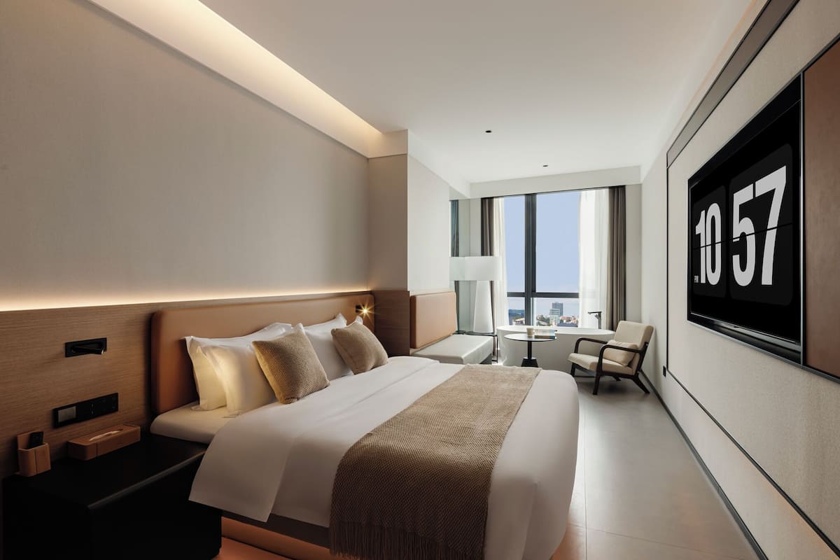 Une chambre d’hôtel moderne, dotée d’un grand lit, de tables de chevet, d’un bureau, d’une chaise et d’un écran de télévision affichant le numéro 1057.