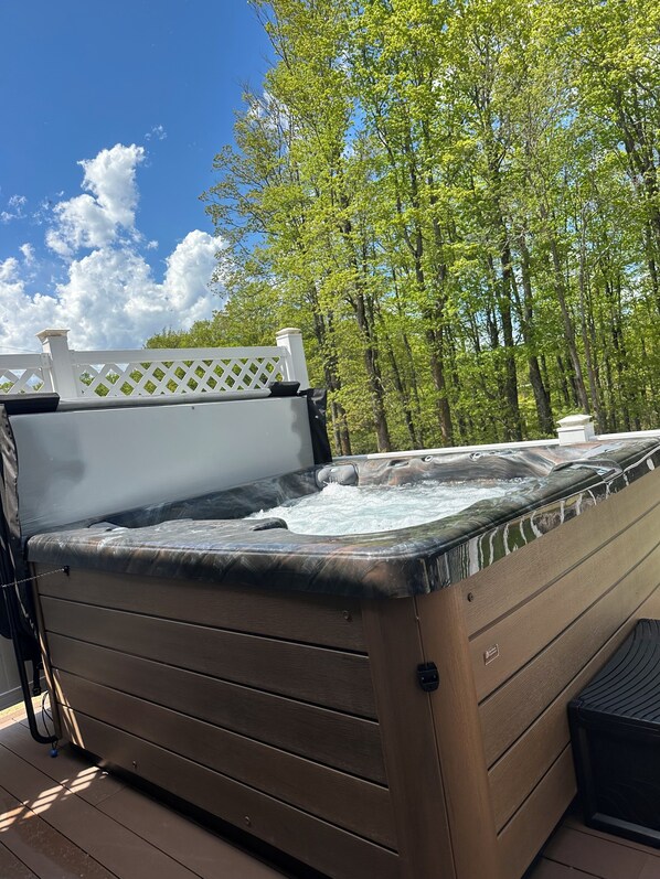 A hot tub on a wooden deck with a white lattice fence and trees in the background. - Trailside#2 TRAILER PARKING/HOT TUB, 2 bed2bath, ATV, snowmobile, ski, snowboard (Wakefield)