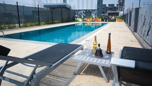 A swimming pool with lounge chairs and a table with bottles and glasses. - Noble Nook Boutique Hotel (Abuja)