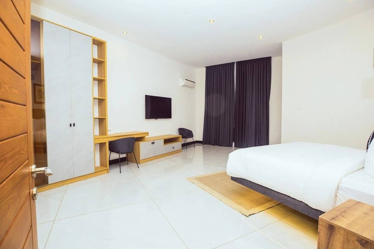 A modern hotel room with a bed, a desk, a chair, a TV, and a wardrobe.