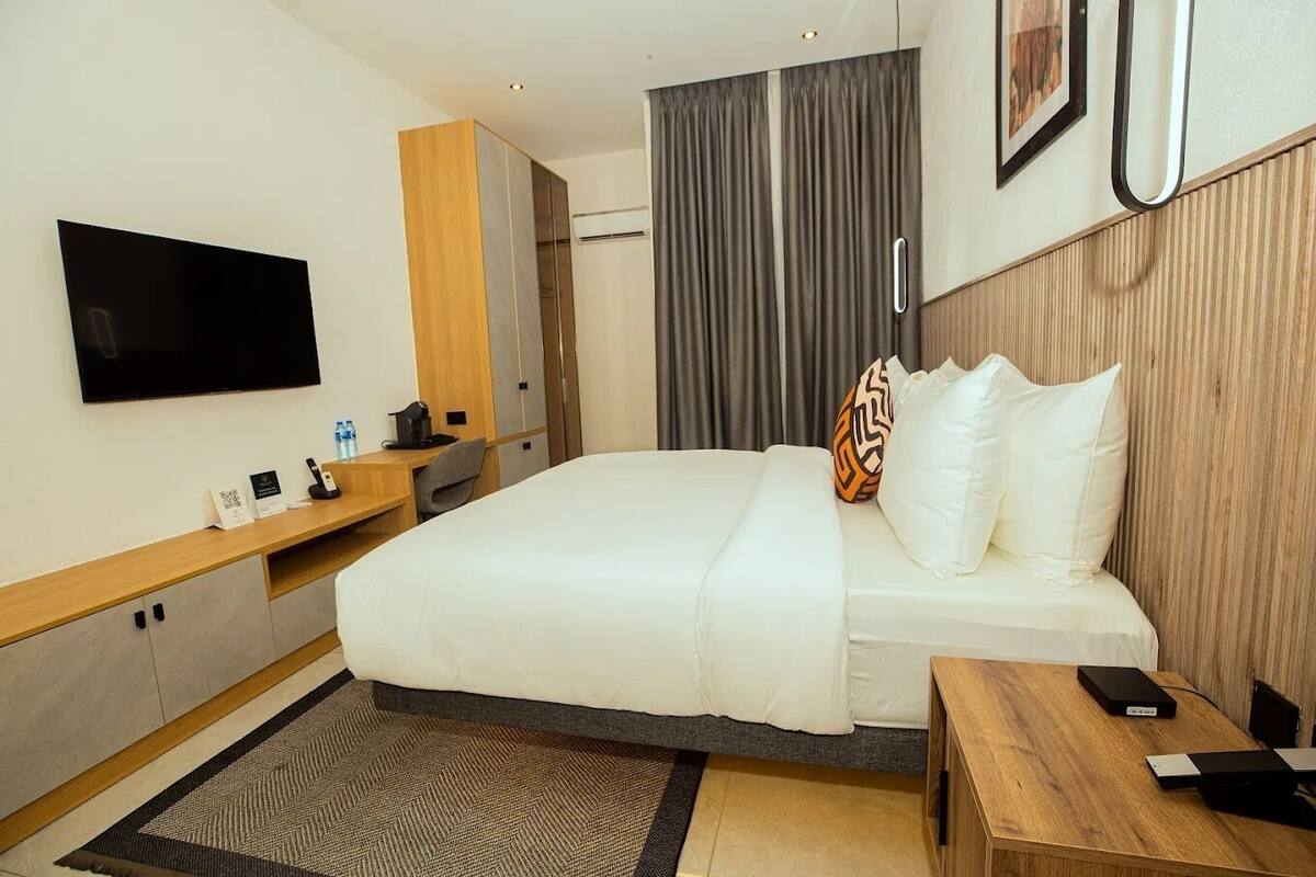 A modern hotel room with a large bed, a desk, a flat-screen TV, and a wooden accent wall.