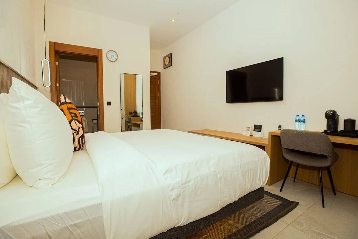 A hotel room with a bed, a desk, a chair, a TV, and a clock on the wall.
