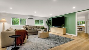 A modern living room with a sofa, a coffee table, a TV, and a dining area visible through an open door. - Secluded White Mtns Retreat • Hot Tub • Sleeps 10 • Pet Friendly (Albany)