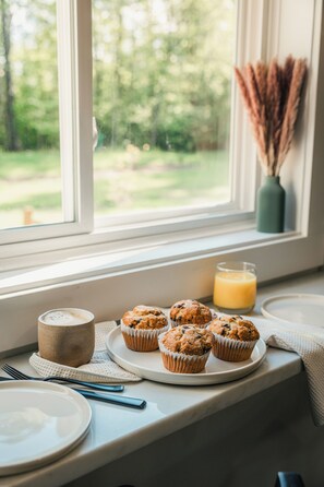 A breakfast setting with muffins, a glass of orange juice, and a rustic mug on a windowsill. - NEW to VRBO! Secluded White Mtns Home•Hot Tub, EV, Pets•Near Kanc Hwy, Sleeps 10 (Albany)