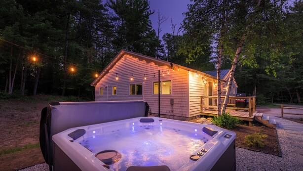 A hot tub in front of a wooden cabin with a deck, surrounded by trees. - Secluded White Mtns Retreat • Hot Tub • Sleeps 10 • Pet Friendly (Albany)