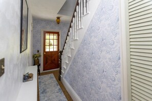A hallway with patterned wallpaper, a wooden door, a staircase with white railings, and a small rug. - Hillside Respite by Sea Maine (Boothbay Harbor)