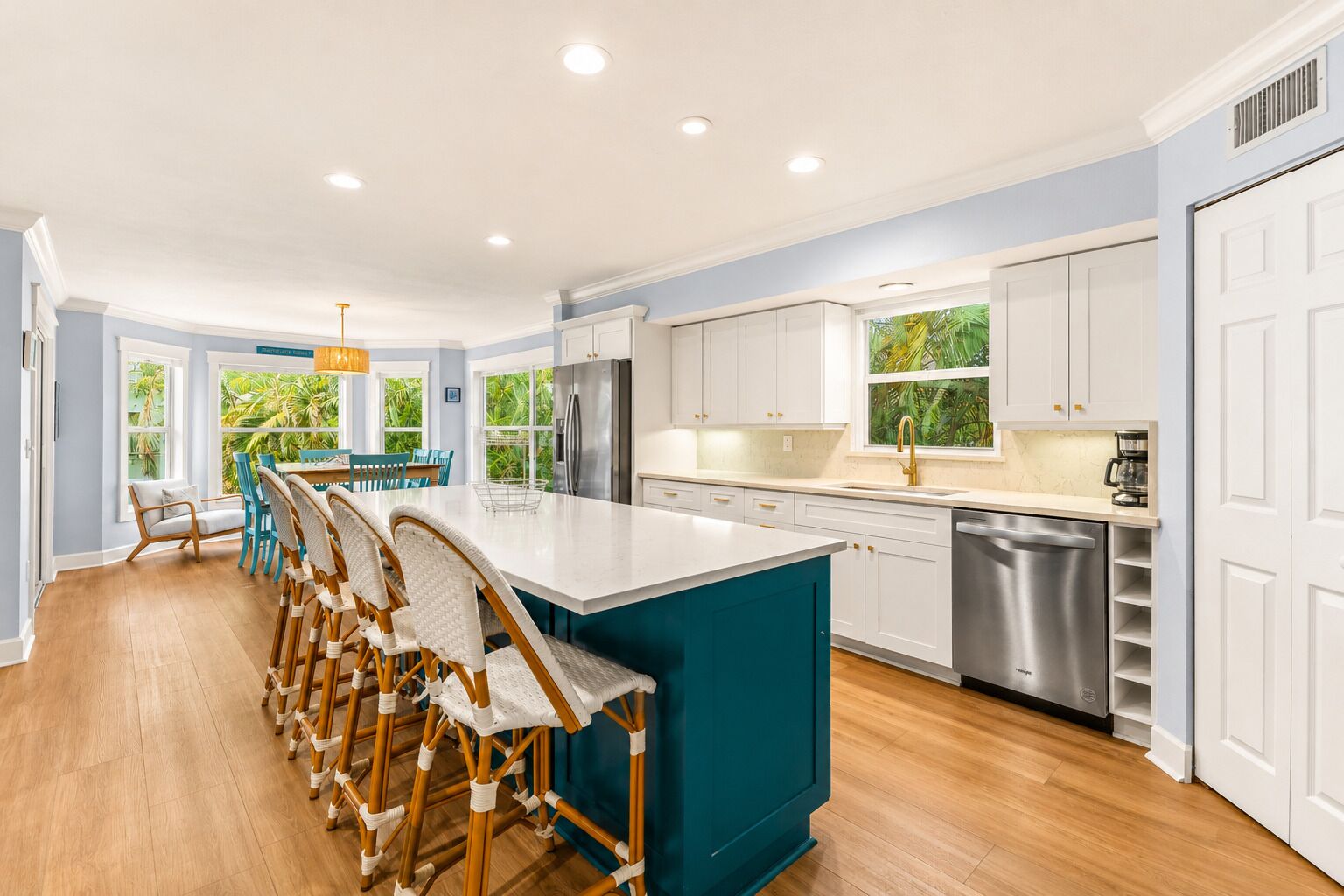 A modern kitchen with a large island, white cabinetry, and a view of greenery outside.