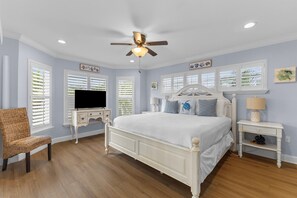A bedroom with a bed, a TV, a ceiling fan, and a chair. - Heated Pool • Hot Tub • Walk to Pine (Anna Maria)