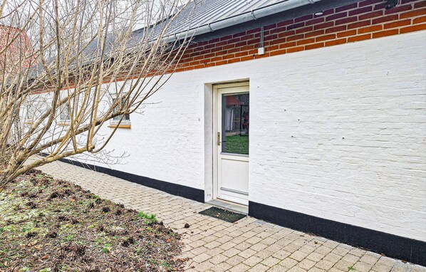 A white building with a red brick section, a door, and a small window. - 1 bedroom cozy apartment in Hjørring (Hjørring)