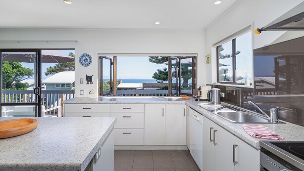 Une cuisine moderne avec des armoires blanches, un comptoir en granit et une vue sur la mer.