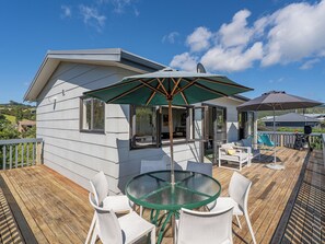 Eine Terrasse mit einem Glastisch, weißen Stühlen, einer Schiebetür und einem grünen Sonnenschirm.