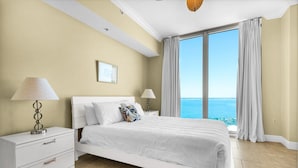 A bedroom with a large bed, two bedside tables, a nightstand, and a view of the ocean. - Portofino Island Resort 3-1705 (Pensacola Beach)