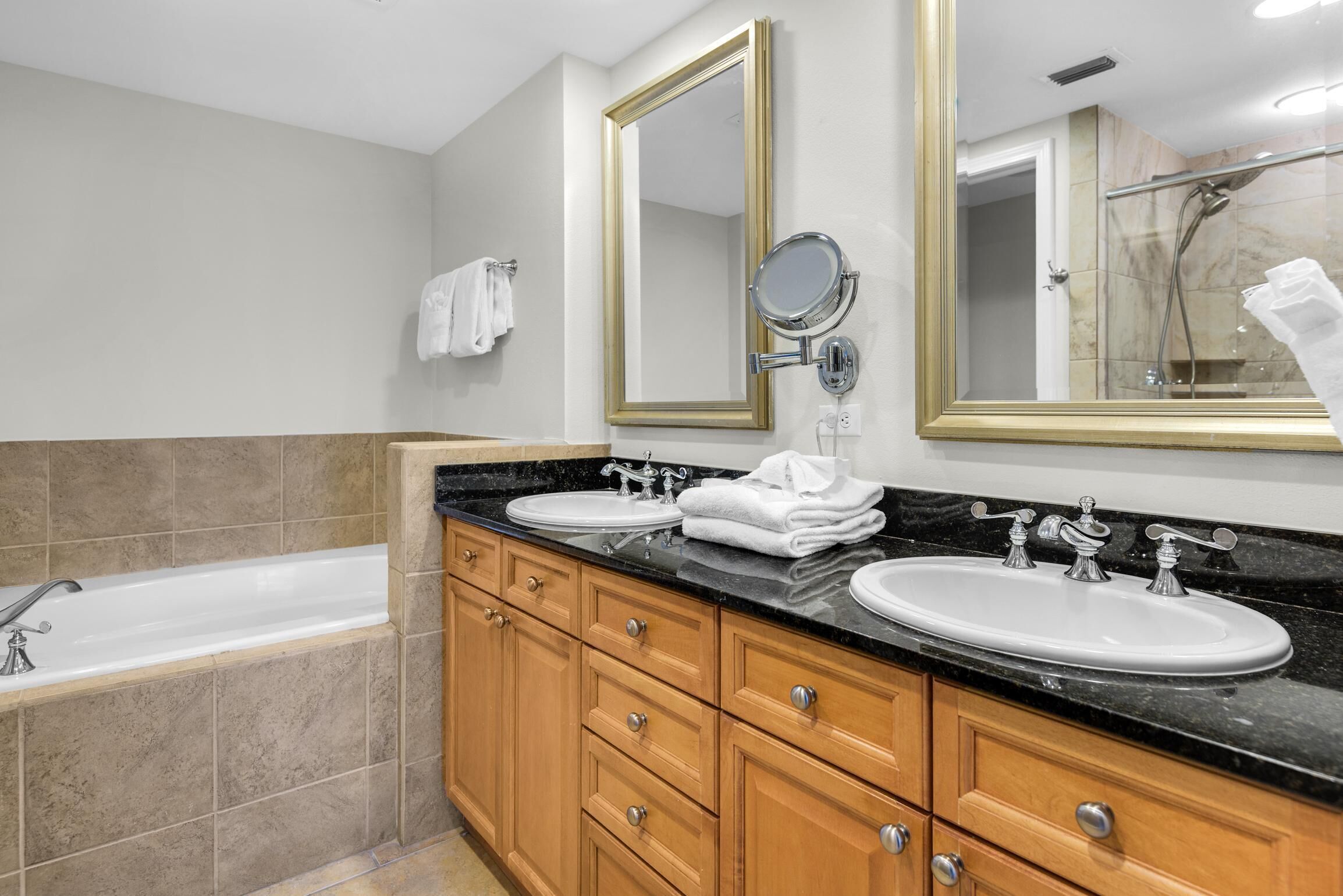 A modern bathroom with a bathtub, two sinks, wooden cabinets, and a large mirror.