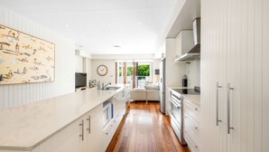 A modern kitchen with white cabinetry, a large island, and a view of the outdoors. - The Shore Thing 1 Peregian Beach (PEREGIAN BEACH)