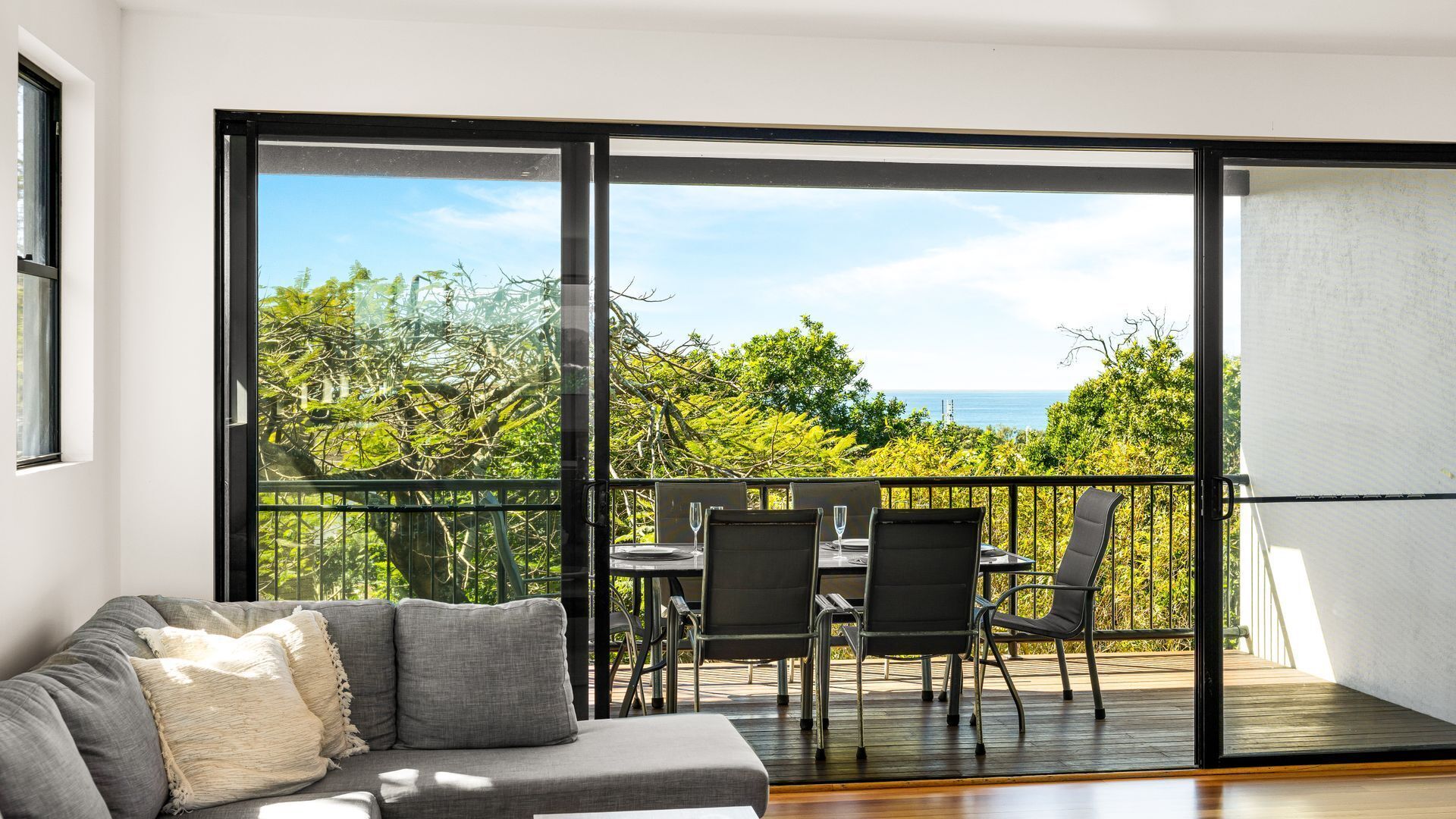 A balcony with a dining table and chairs, overlooking a lush green landscape and the sea.
