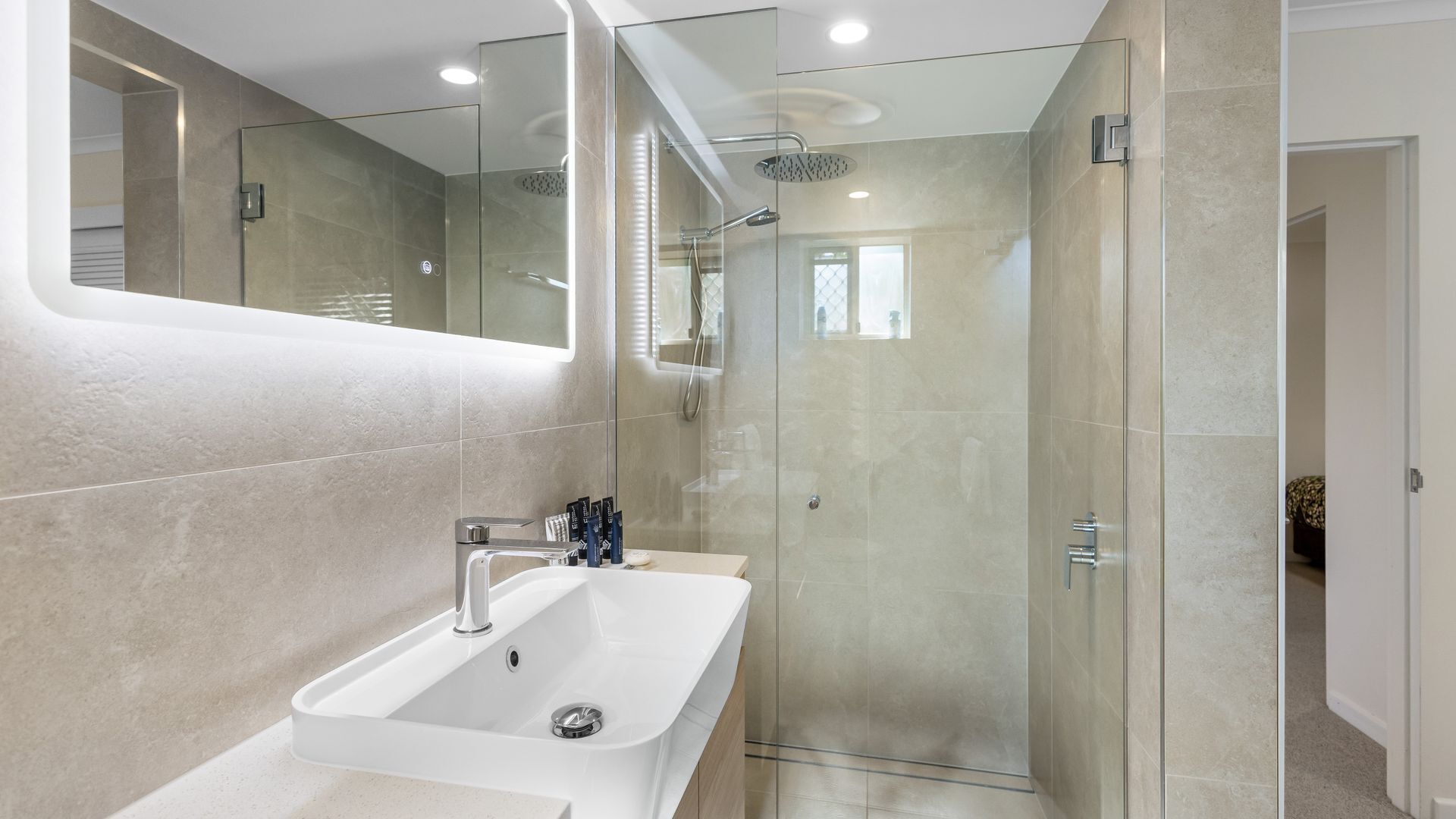 A modern bathroom with a glass-enclosed shower, a white sink, and a large mirror.