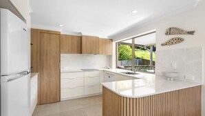Cocina moderna con armarios de madera, encimera blanca y un amplio ventanal con vistas a zonas verdes.