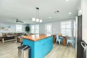 A modern kitchen with a blue island, a dining area with a table and chairs, and a living room with a sofa and a coffee table. - License to Chill - Your Official Permit to Relax! (Surfside Beach)