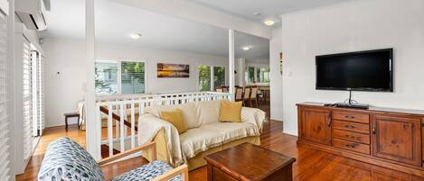 A spacious living area with a sofa, patterned armchair, wooden coffee table, and a TV on a wooden cabinet.