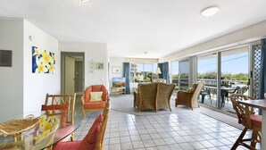 Un'ampia zona giorno con balcone, mobili in vimini e un tavolo da pranzo in vetro.