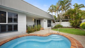 Ein Wohnhaus mit Swimmingpool, überdachter Terrasse und umzäunter Garten mit Palmen.