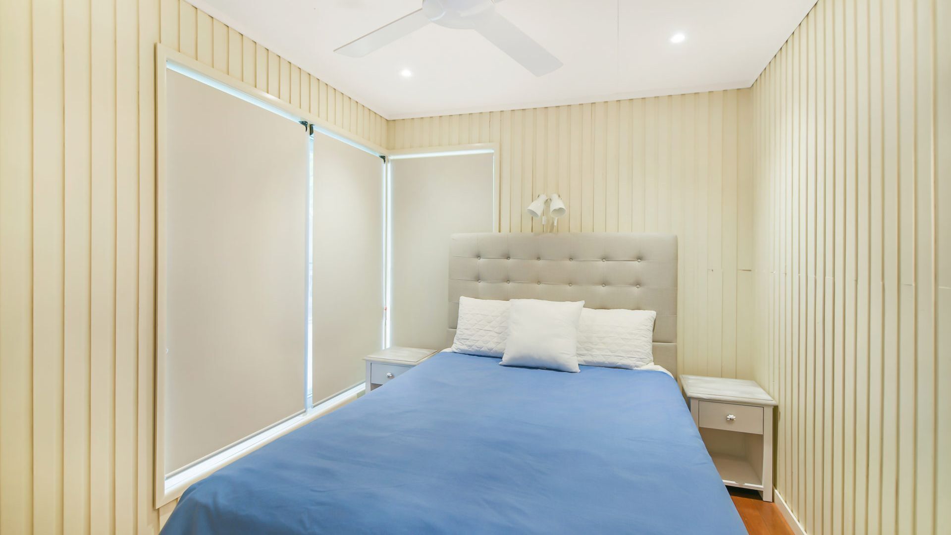 A bedroom with a bed, nightstands, a ceiling fan, and a window with blinds.
