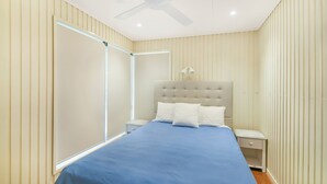 A bedroom with a bed, nightstands, a ceiling fan, and a window with blinds. - Summer Place on Shearwater Peregian Beach (PEREGIAN BEACH)