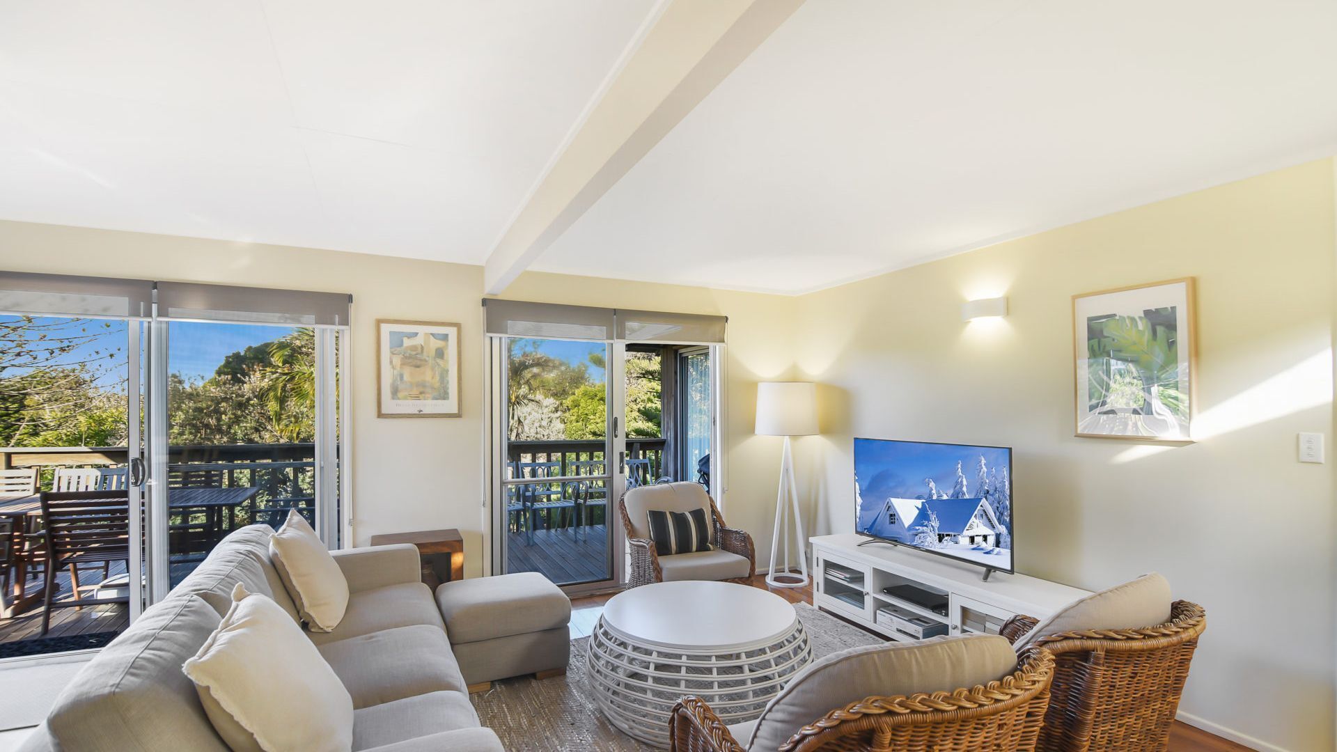 Amplia sala de estar con sofá, reposapiés y sillas de mimbre, televisor de pantalla plana y balcón con mobiliario exterior.