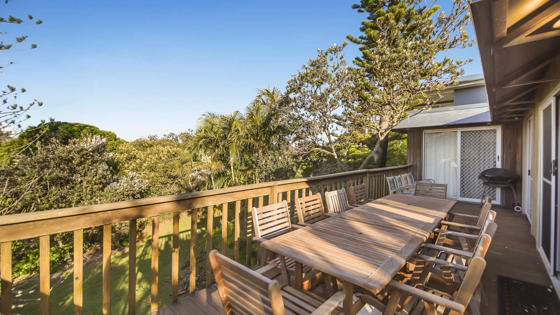 A wooden deck with a dining table and chairs, surrounded by lush greenery and trees.