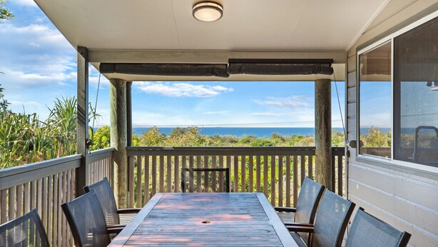Un patio techado con una mesa y sillas, con vistas panorámicas al océano.