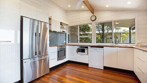 Cocina moderna con electrodomésticos de acero inoxidable, piso de madera y un amplio ventanal con vistas a árboles.