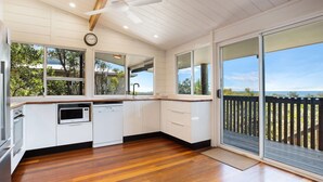 Una cocina con armarios blancos, microondas, lavavajillas y encimera de madera. Cuenta con un ventanal con vistas a árboles y una terraza exterior.