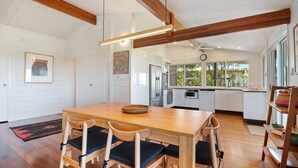 Una cocina amplia con armarios blancos, un refrigerador de acero inoxidable y un microondas. Hay una mesa de comedor de madera con sillas y una cesta tejida encima.