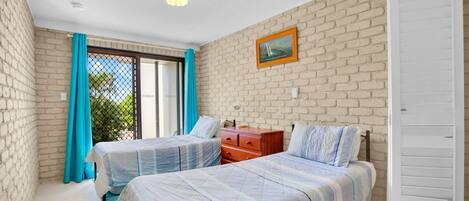 A bedroom with two beds, a wooden dresser, a white wardrobe, and a brick wall.