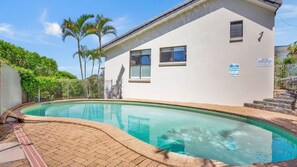 A swimming pool with a curved edge, a white building with windows, and a metal fence. - Galleries 3 Peregian Beach (Peregian Beach)