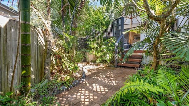 A tropical garden with a wooden fence, a stone pathway, and a staircase leading to a building. - Woodside on Brolga 3 Peregian Beach (PEREGIAN BEACH)