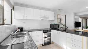 A modern kitchen with white cabinets, a black countertop, a stove, an oven, and a sink. - Woodside on Brolga 3 Peregian Beach (PEREGIAN BEACH)