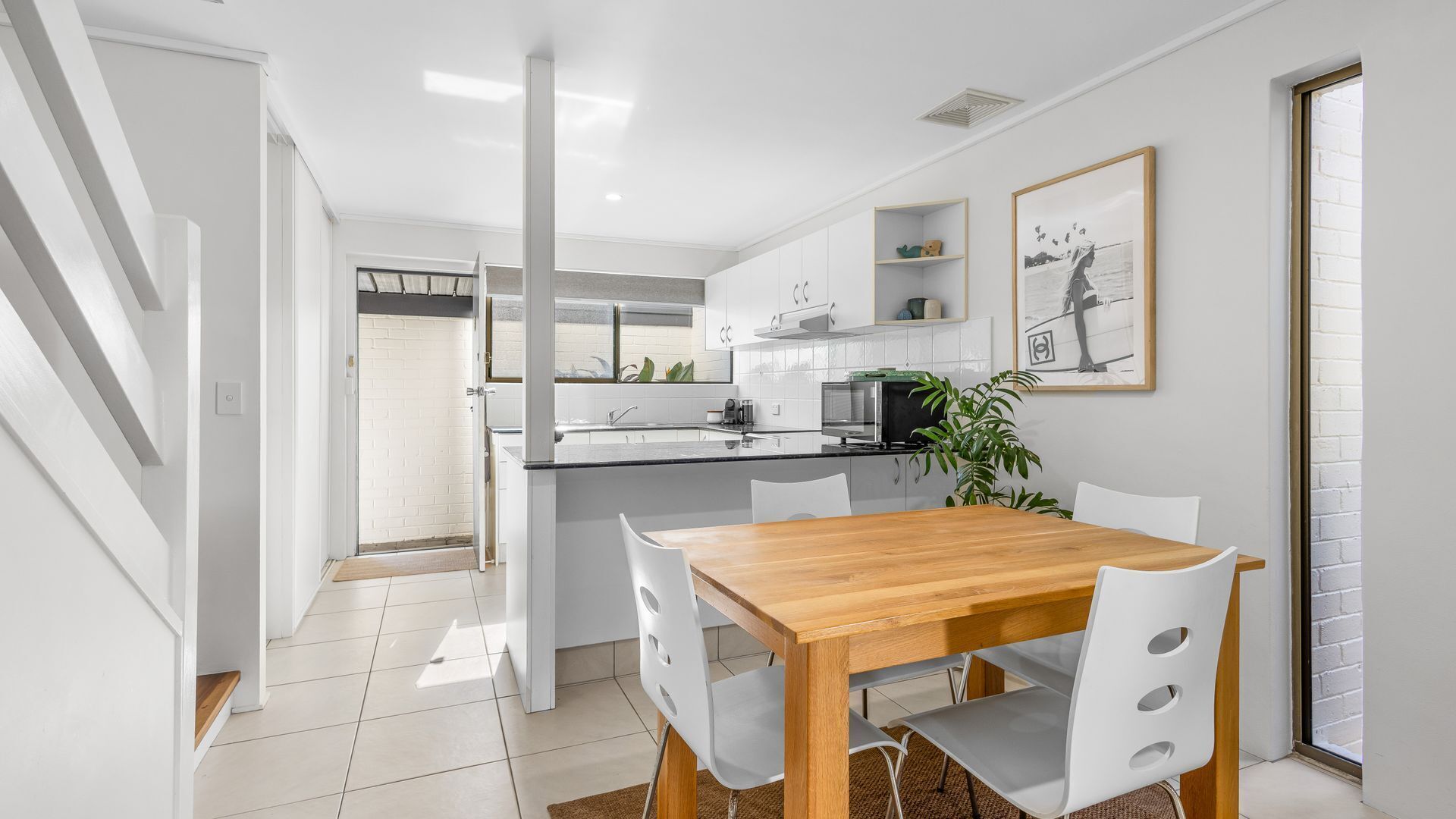 Una cocina moderna con armarios blancos, una mesa de comedor con sillas y una planta.