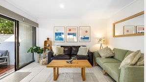 A modern living room with a leather sofa, a green sofa, a wooden coffee table, and framed artwork on the wall. - Woodside on Brolga 3 Peregian Beach (PEREGIAN BEACH)