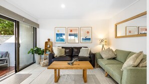 Ein modernes Wohnzimmer mit einem Ledersofa, einem grünen Sofa, einem Holztisch und gerahmten Kunstwerken an der Wand.