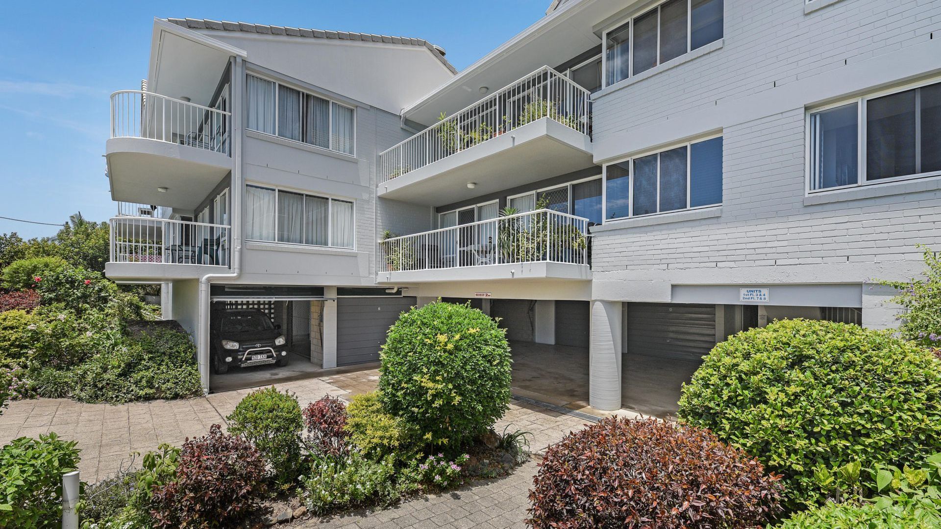En flervåningsbostadsbyggnad med balkonger, ett garage och en välskött trädgård.