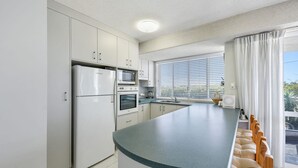 Una cocina moderna con armarios blancos, horno empotrado, refrigerador y una isla grande con pileta.