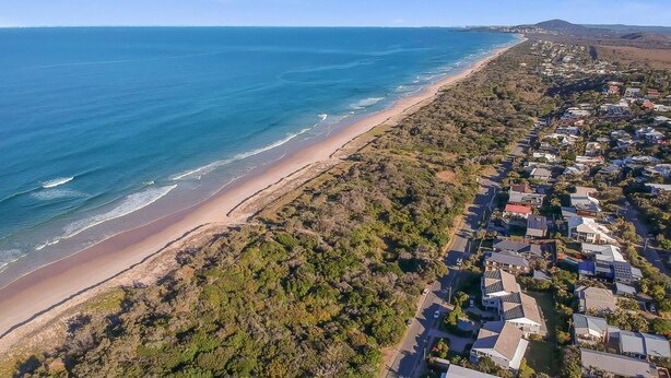 Vista aérea de una zona residencial costera con playa, casas y vegetación.
