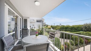Un balcón con mesa y sillas, con vistas a un jardín y edificios vecinos.