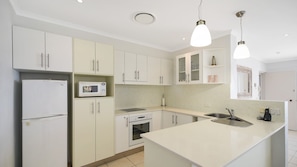 A modern kitchen with white cabinets, a built-in microwave, a stove, and a large island with a sink. - Kari 3 Peregian Beach (PEREGIAN BEACH)