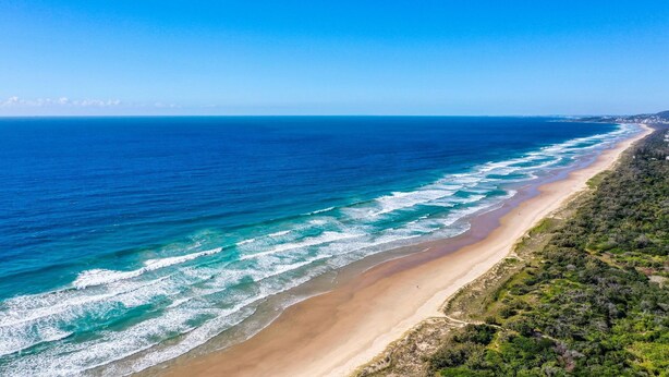 Paesaggio costiero con spiaggia sabbiosa e onde oceaniche.