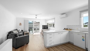 A modern kitchen with white cabinets, a built-in dishwasher, and a window overlooking the balcony. - Blairgowrie 4 Peregian Beach (PEREGIAN BEACH)