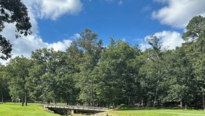 Un parc avec un pont de pierre enjambant un petit ruisseau, entouré d’une végétation luxuriante et d’arbres.